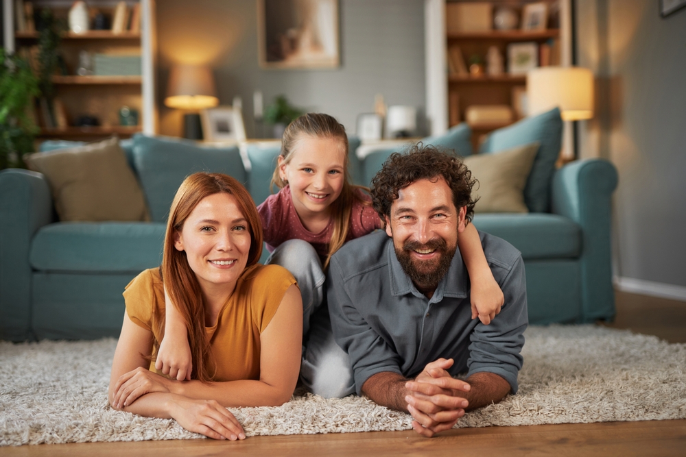 Happy Family Relaxing in Cozy Living Room – Sell My House Oceanside Smiling family of three relaxing on the floor in their bright living room, symbolizing a new beginning – Sell My House Oceanside