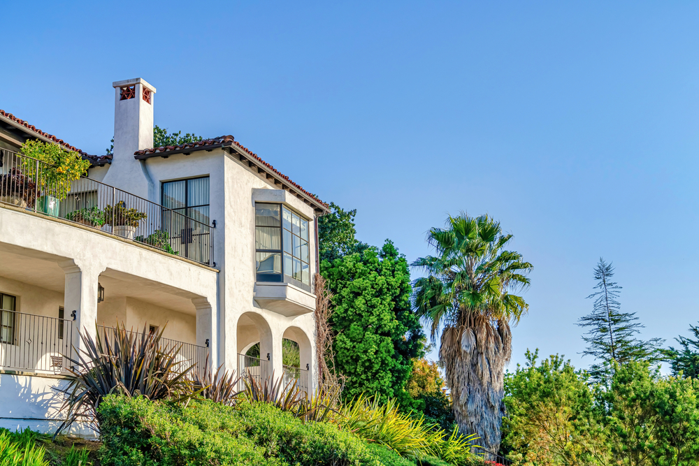 Hillside Mediterranean-style home surrounded by lush landscaping and palm trees, representing homeowners looking to sell property quickly and easily in San Diego - JP Buys SD