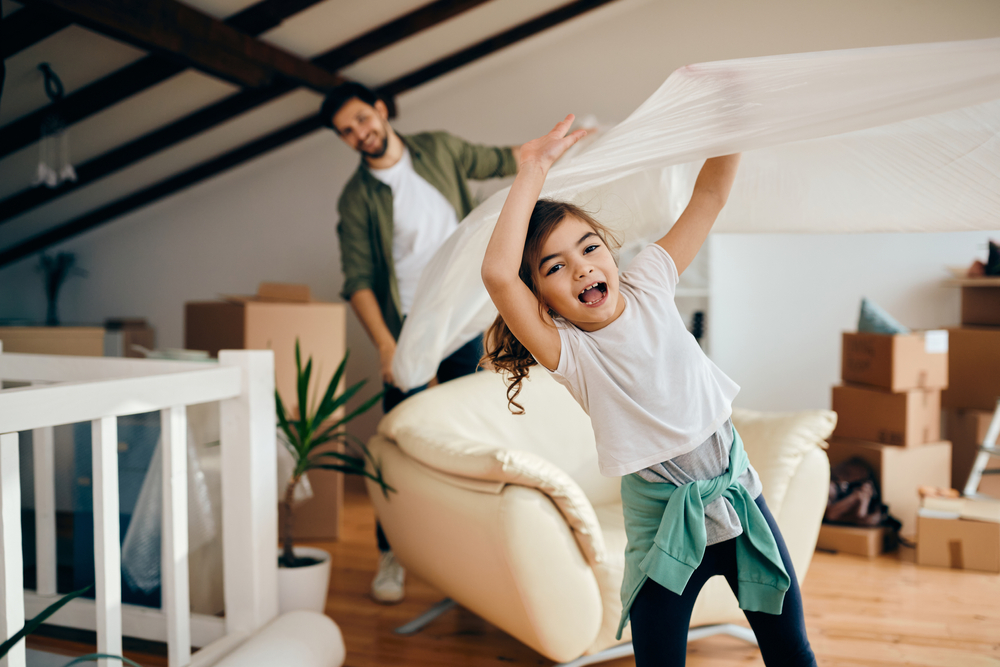 Happy Family Moving Into New Home – We Buy Houses Richland Excited young girl playing while moving into a new house with her father unpacking boxes in the background – We Buy Houses Richland