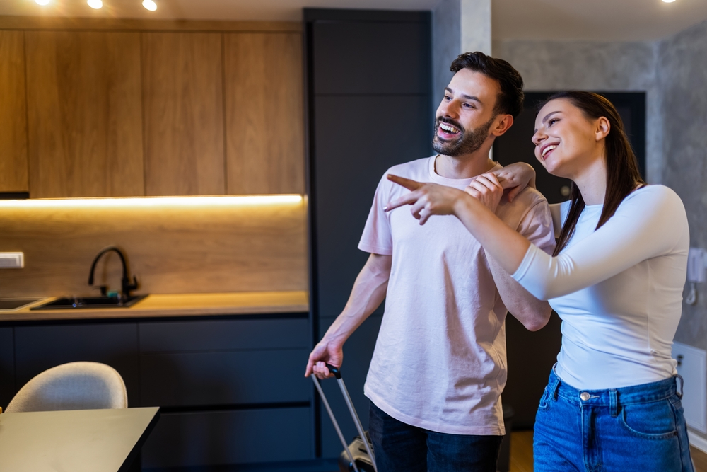 Smiling couple standing in a modern kitchen and pointing excitedly while viewing a new home, representing successful home sales and quick real estate transactions – Sell My House Fast El Cajon