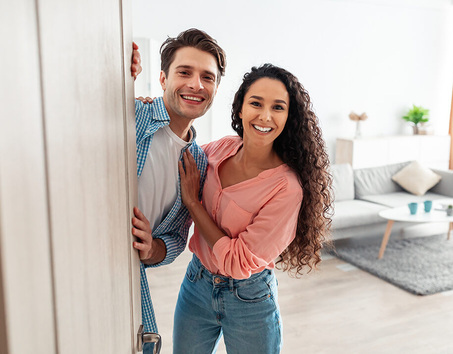 Happy Couple Entering New Home – Sell My House Fast Spring Valley CA Smiling couple standing at their new home entrance after completing a quick home sale – Sell My House Fast Spring Valley CA