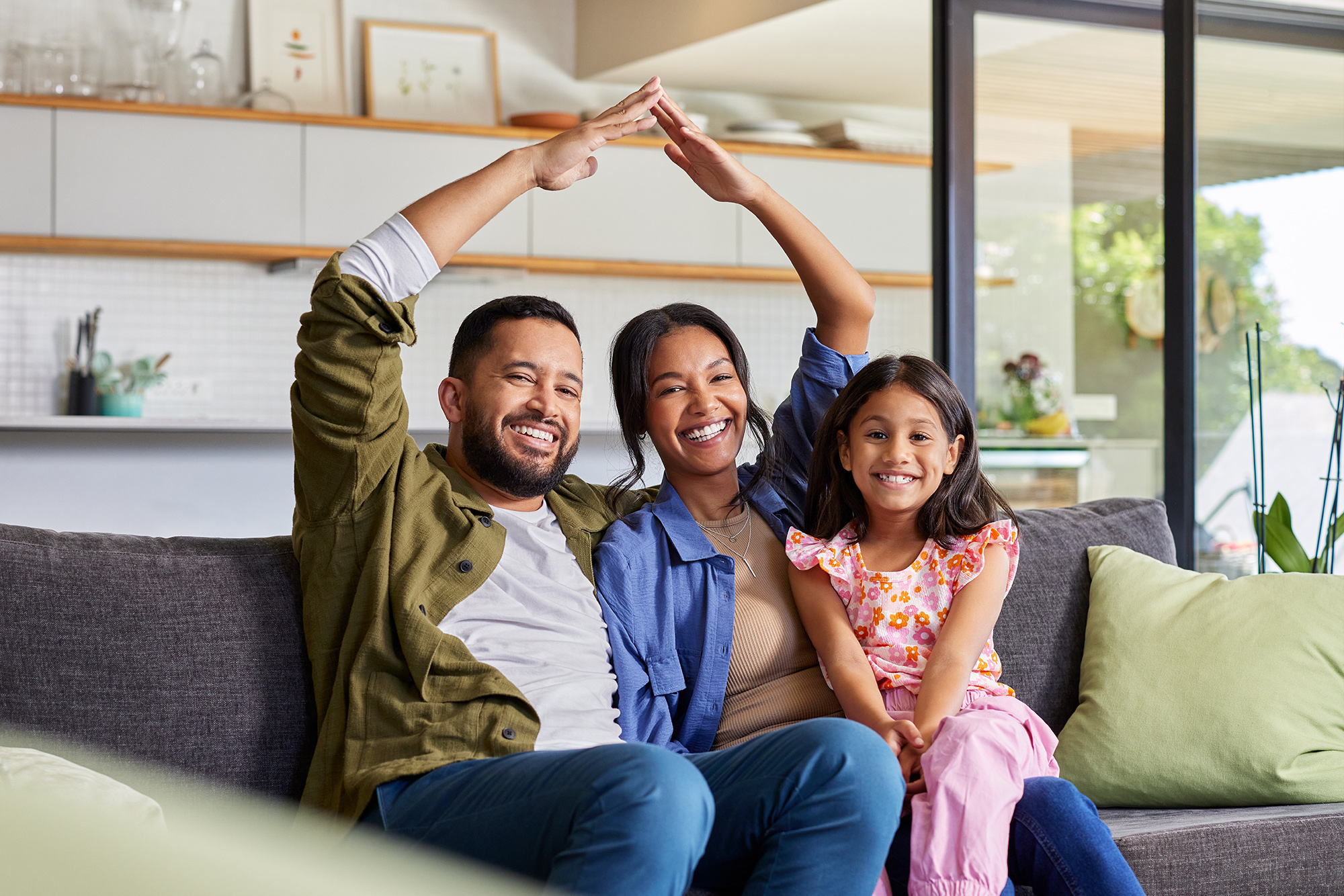 Happy Family Relaxing in Their New Home – We Buy Houses Vista Smiling family sitting together on the couch forming a roof shape with their hands, celebrating a fast and successful home sale in Vista – We Buy Houses Vista
