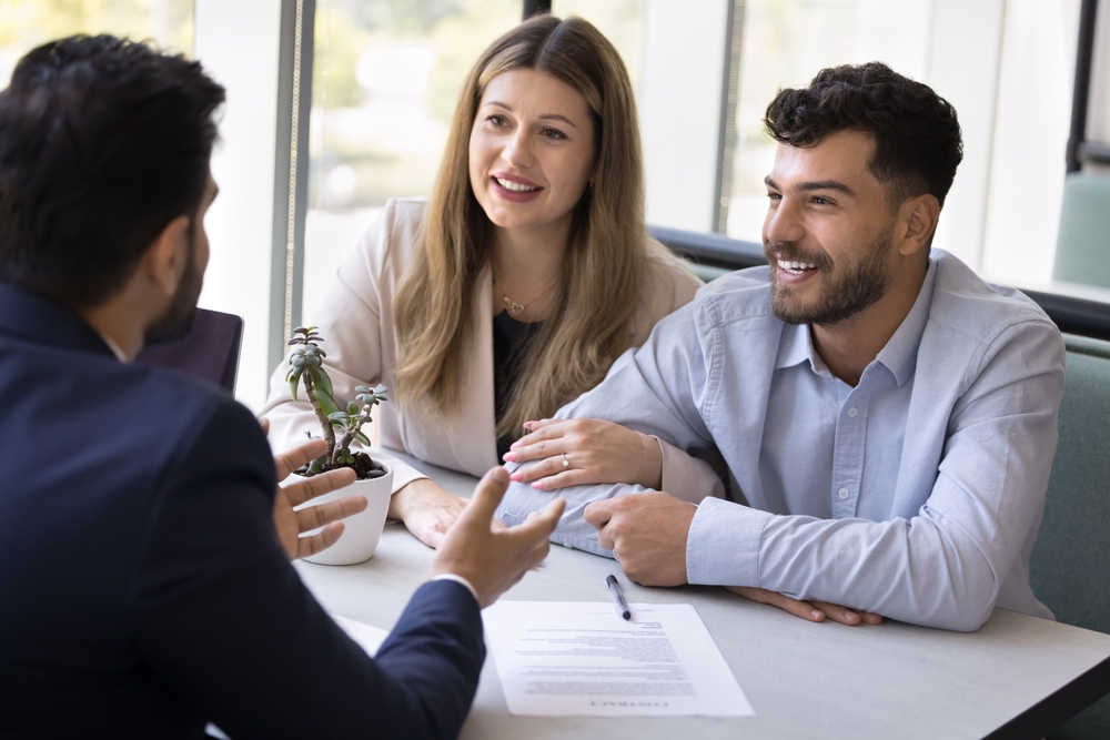Smiling couple discussing paperwork with a real estate agent in an office, representing an easy home-selling process – We Buy Houses Chula Vista