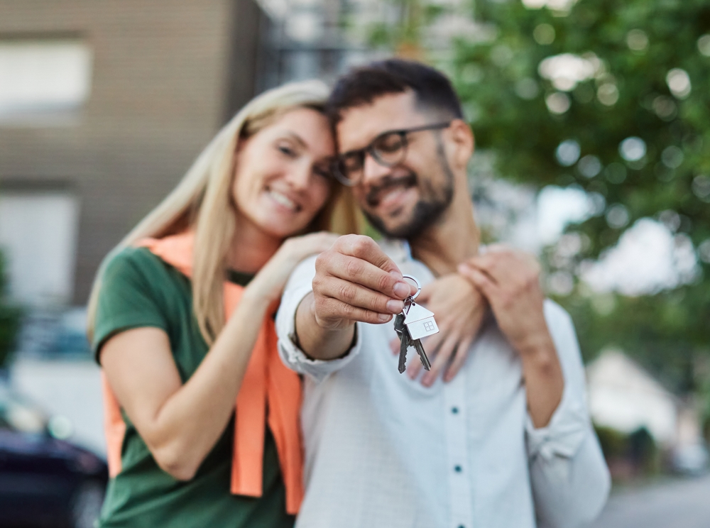 Smiling couple celebrating their new home purchase while holding house keys outdoors, symbolizing successful real estate transactions – Mission Valley Home Buyers