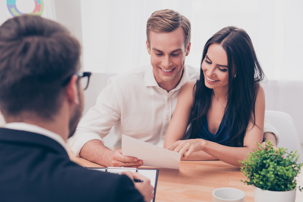 Happy Couple Discussing Property Sale with Agent – Sell My House Fast San Diego Smiling couple reviewing real estate documents with a professional agent during a home selling consultation, representing quick and successful property sales – Sell My House Fast San Diego