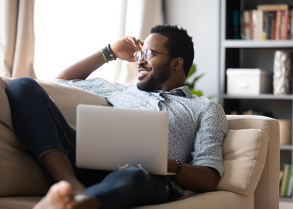 Relaxed Homeowner After Quick Sale – Sell My House Fast Spring Valley CA Smiling man sitting on couch with laptop feeling relieved after selling his home quickly – Sell My House Fast Spring Valley CA