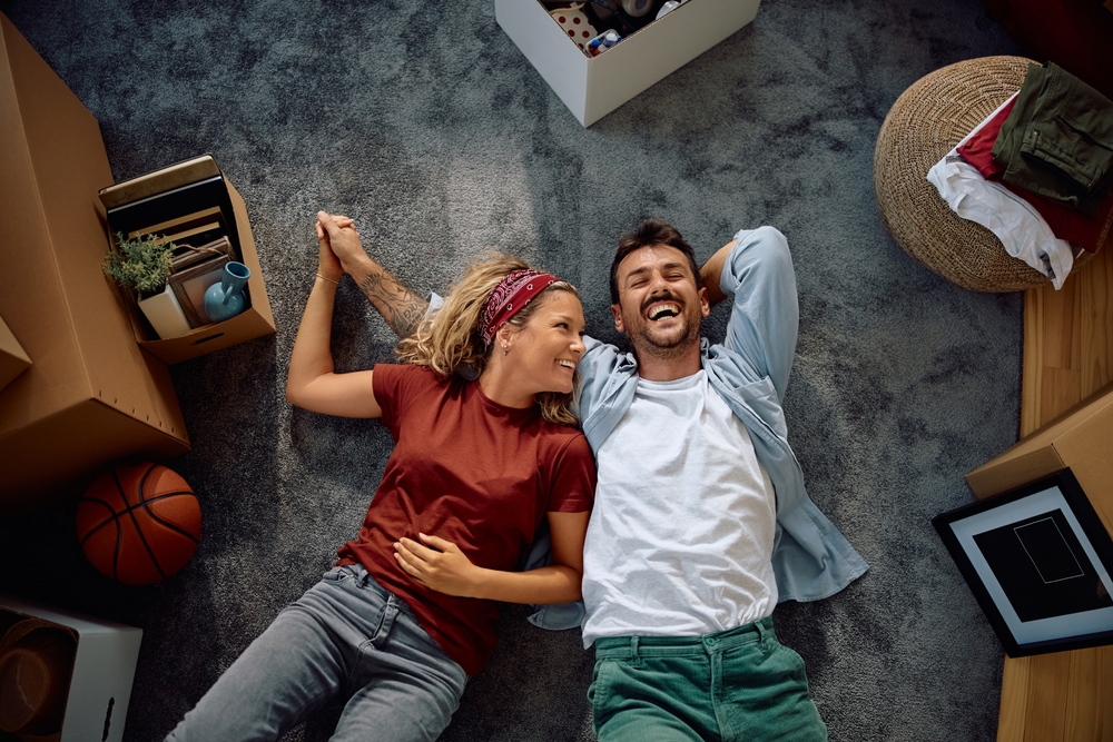 Happy Couple Relaxing After Moving – We Buy Houses Richland Smiling couple lying on the floor surrounded by moving boxes, celebrating a fresh start after selling their home – We Buy Houses Richland