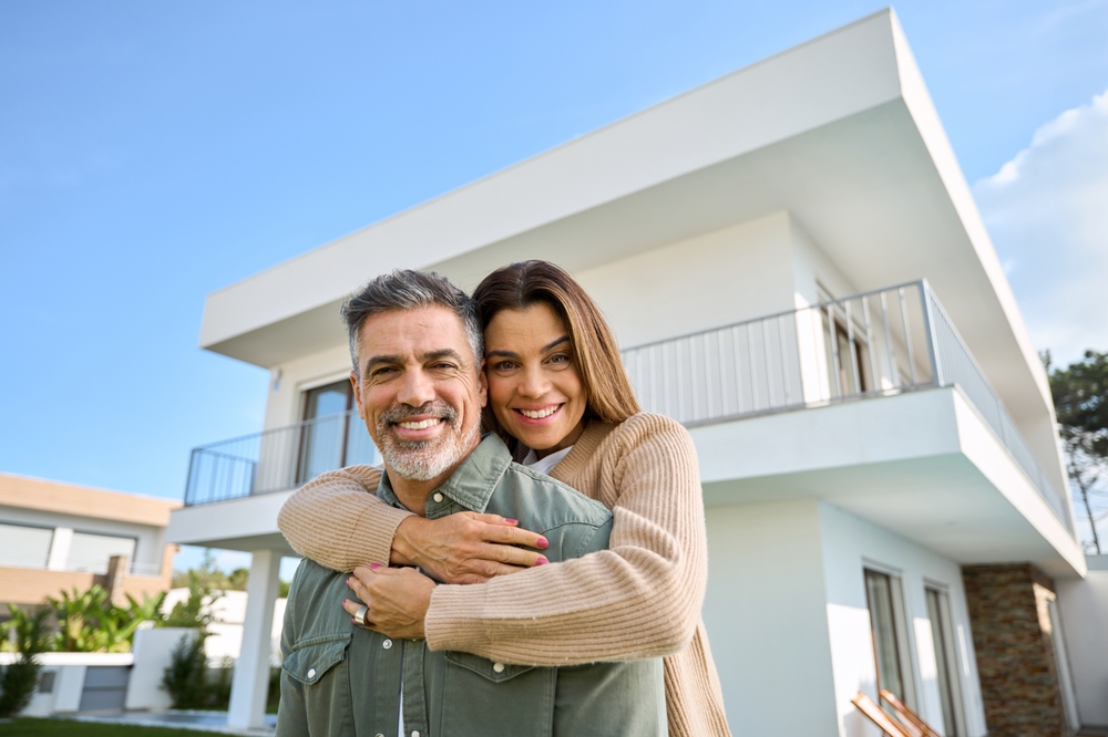 Smiling couple embracing outside a modern two-story home, symbolizing a successful and stress-free home sale – We Buy Houses Chula Vista