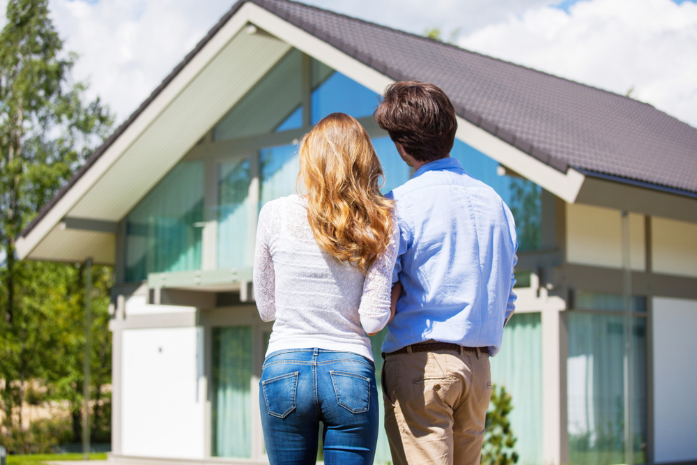 Couple Looking at Their New Home – Sell My House Fast Escondido Rear view of a happy couple standing together and admiring their modern new home under a bright sky, representing a smooth and successful home sale – Sell My House Fast Escondido