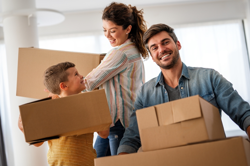 Happy Family Moving Boxes – Sell My House Oceanside Smiling family carrying moving boxes inside their new home, representing a smooth home sale experience – Sell My House Oceanside