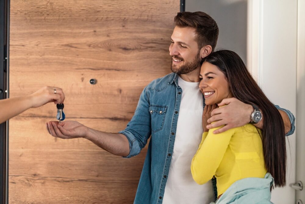 Happy Couple Receiving House Keys – Sell My House Fast Escondido Smiling couple standing at their new home’s doorway receiving house keys, symbolizing a successful and stress-free home sale – Sell My House Fast Escondido