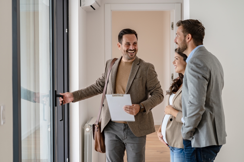 Smiling real estate agent showing a modern home to a couple during a walkthrough, symbolizing trusted and professional home-buying services – Mission Valley Home Buyers
